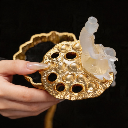 Decorative gold object with a white figurine held by a hand against a black background