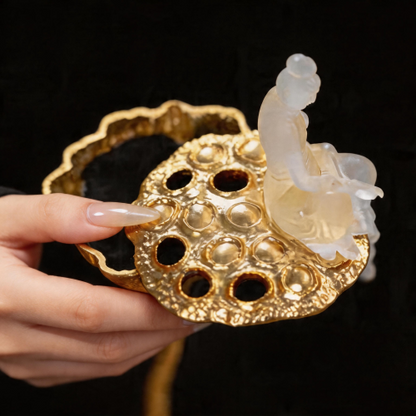Decorative gold object with a white figurine held by a hand against a black background