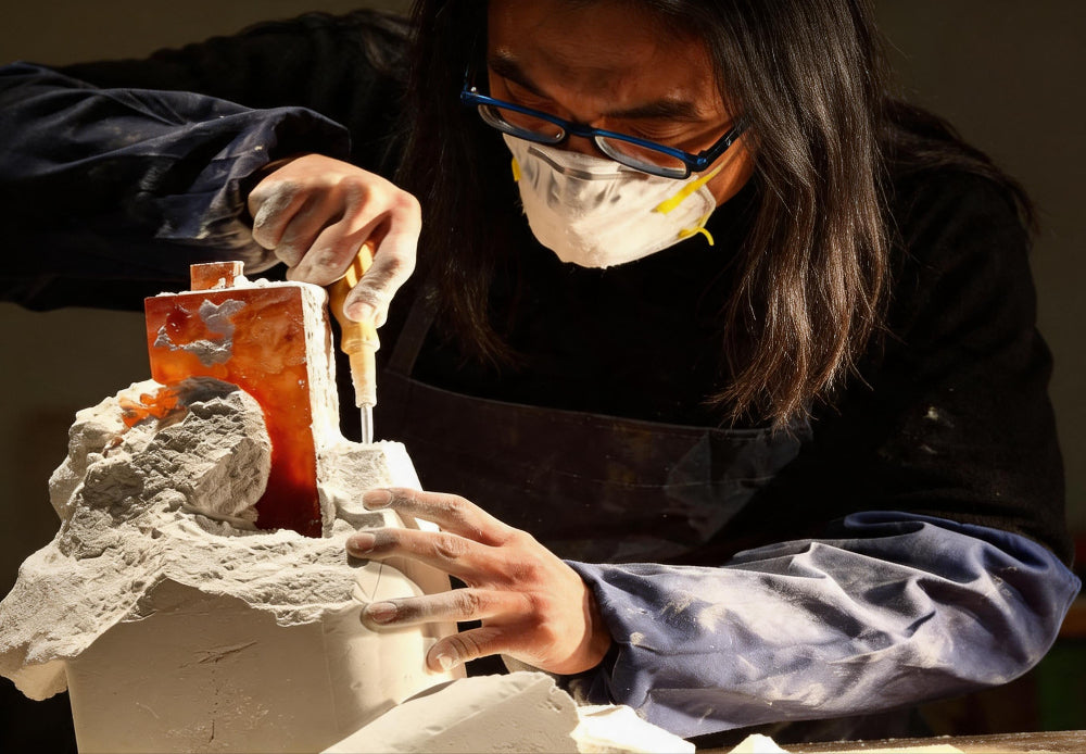 Person working on a sculpture with tools, wearing protective gear.